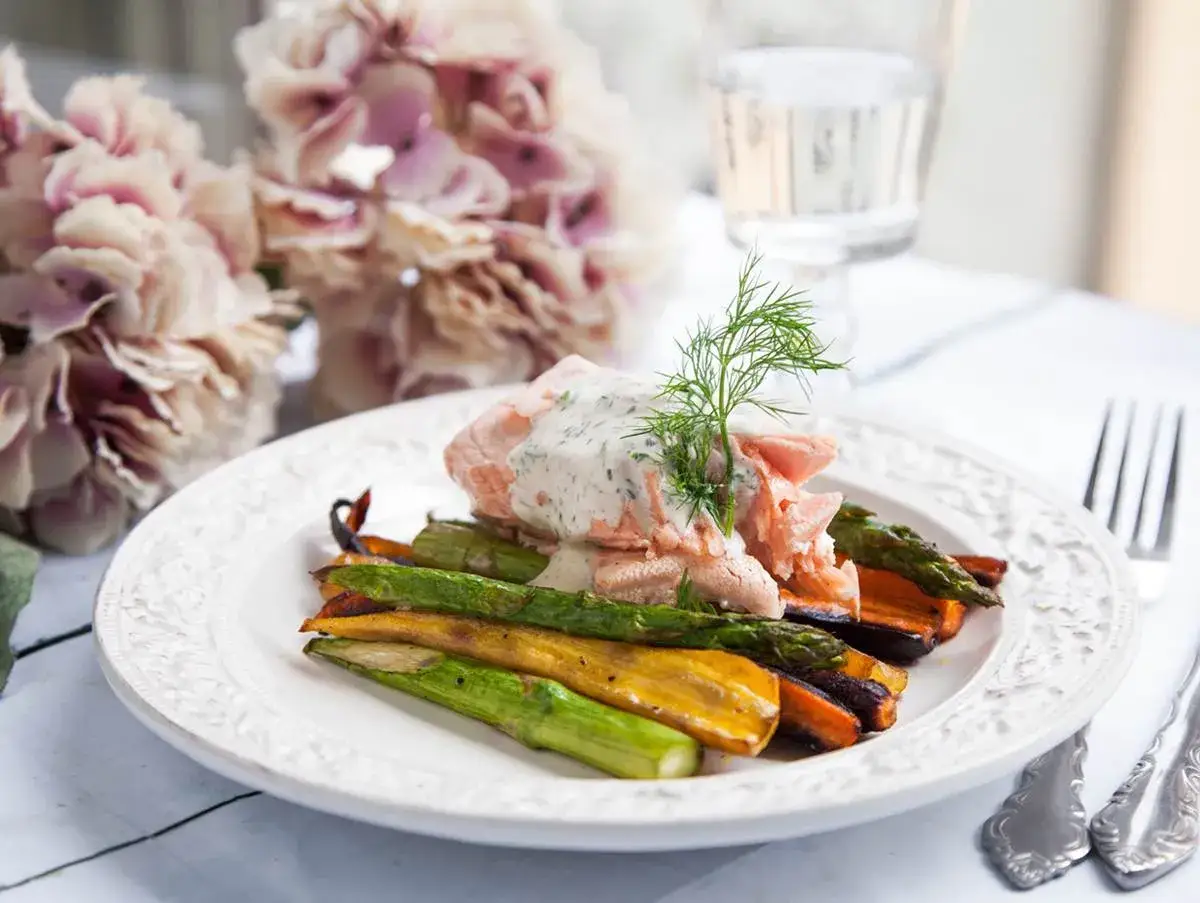 En portion inkokt lax med krämig sås, serverad med rostade rotfrukter och sparris. En vacker och smakrik rätt.