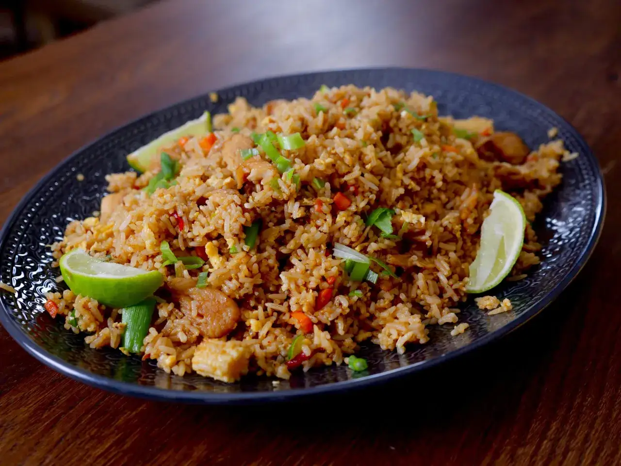 En tallrik med stekt ris, kyckling, grönsaker och limeklyftor. Ett perfekt fried rice recept för en snabb och god middag.