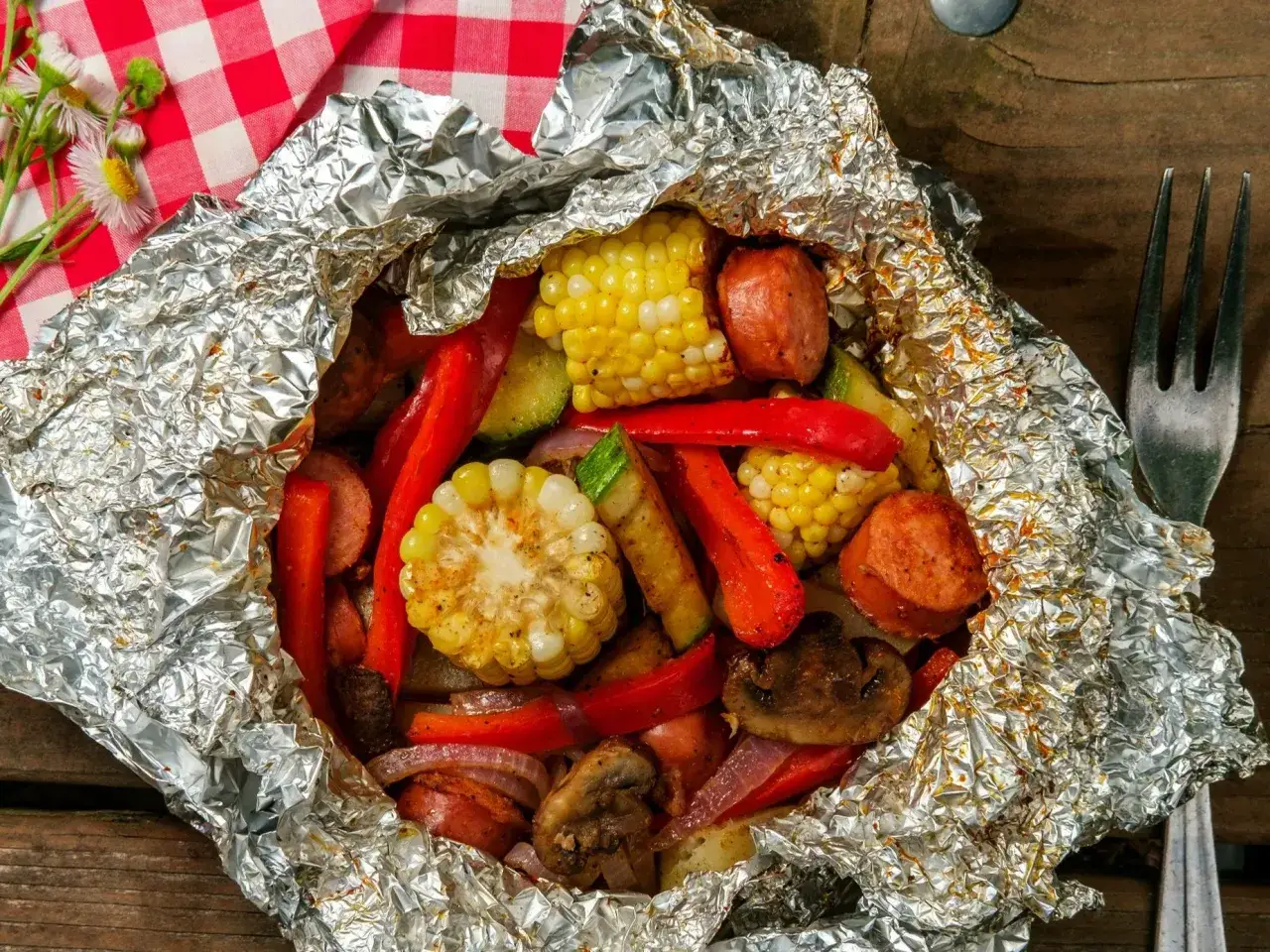 Pyszna kiełbasa na grilla z warzywami w folii aluminiowej: kukurydza, papryka, cukinia i pieczarki.
