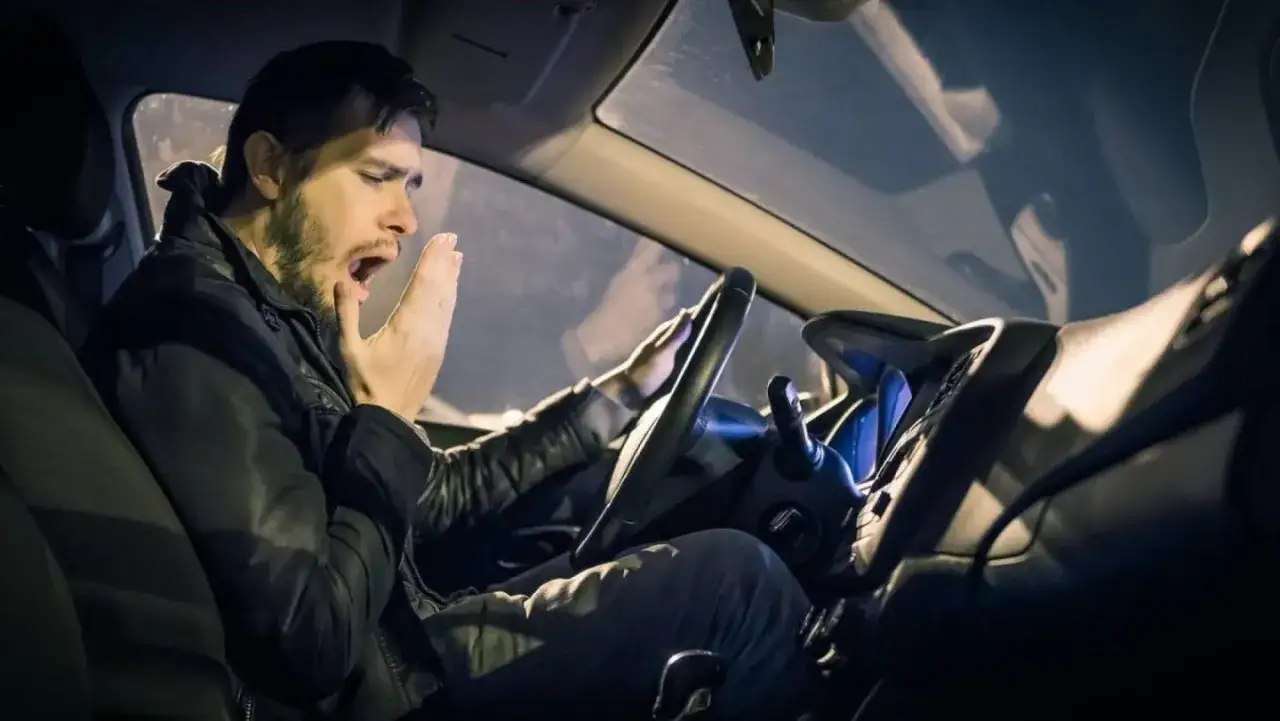Hombre bostezando al volante, mostrando cómo el sueño y la fatiga influyen en la conducción.
