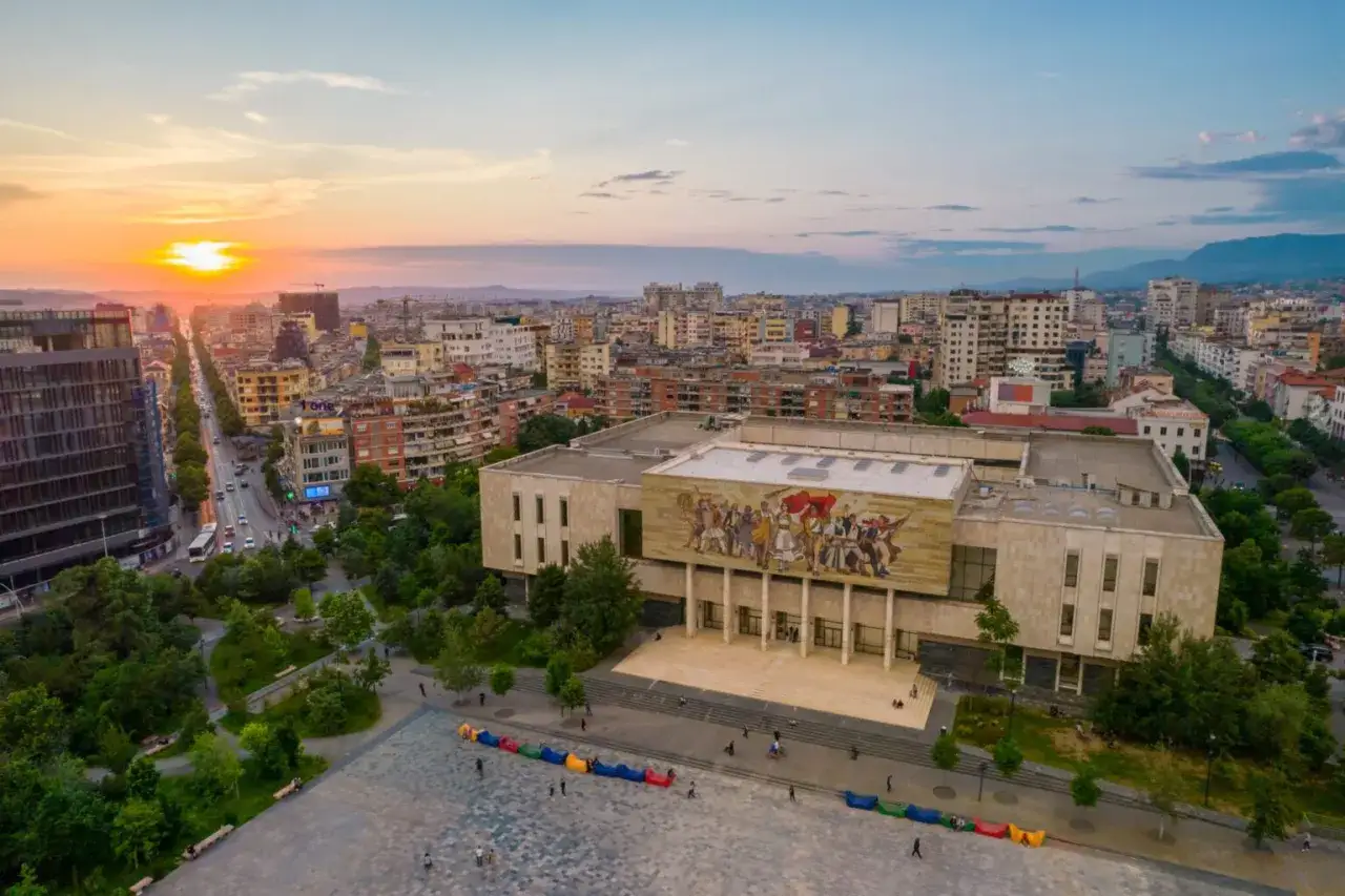 Zachód słońca nad stolicą Albanii, Tirana. Widok na plac z kolorowymi pufami i budynek z mozaiką.