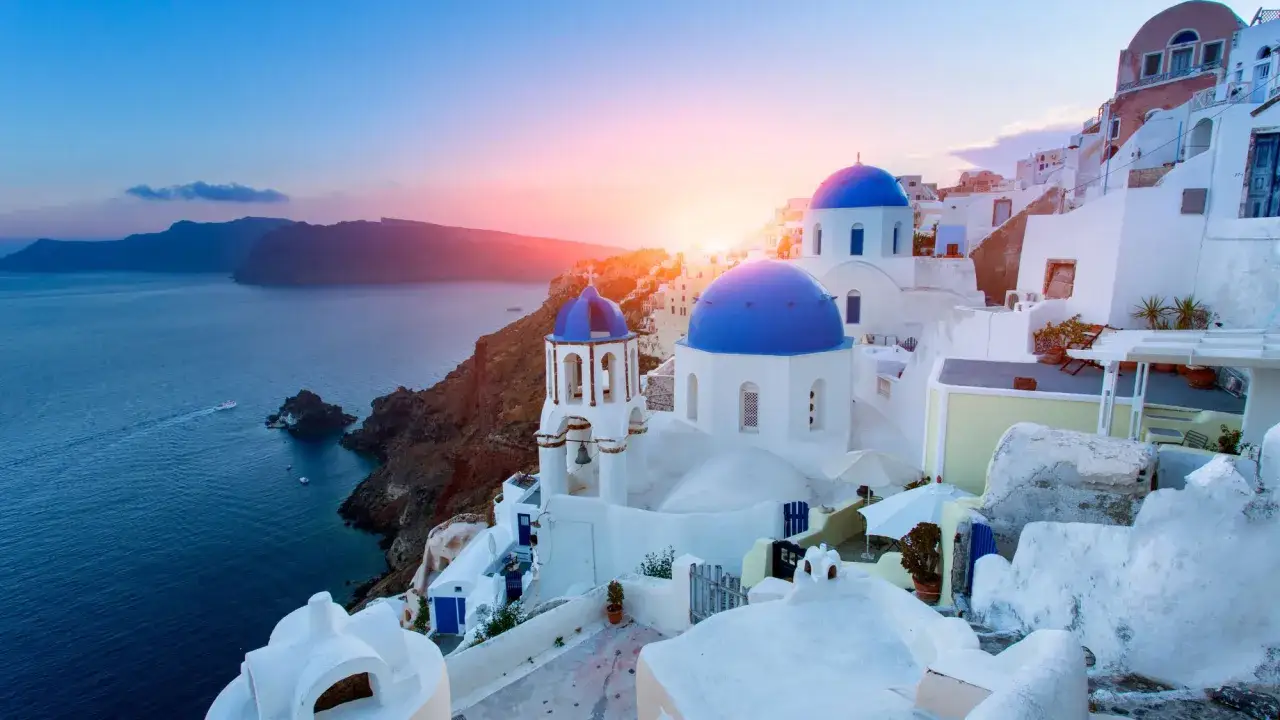 Zachód słońca nad Santorini. Białe domy i niebieskie kopuły kościołów na tle morza. Idealne miejsce na wakacje.