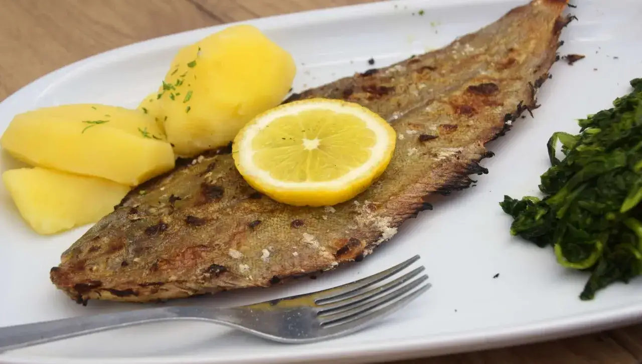 Delicioso lenguado al horno con patatas cocidas y espinacas. Una rodaja de limón corona el pescado.
