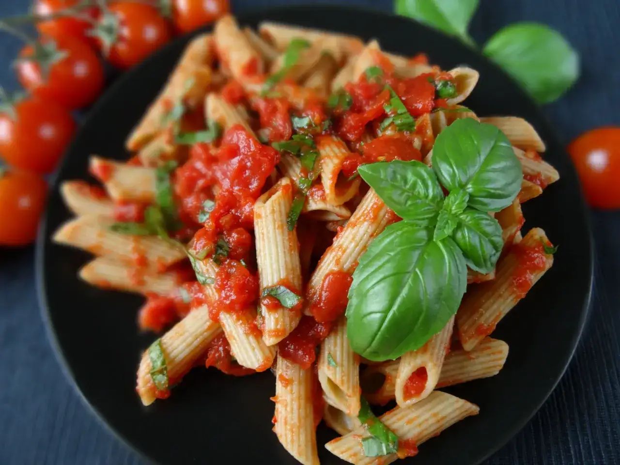 Penne z sosem pomidorowym i świeżą bazylią, ozdobione pomidorkami koktajlowymi.