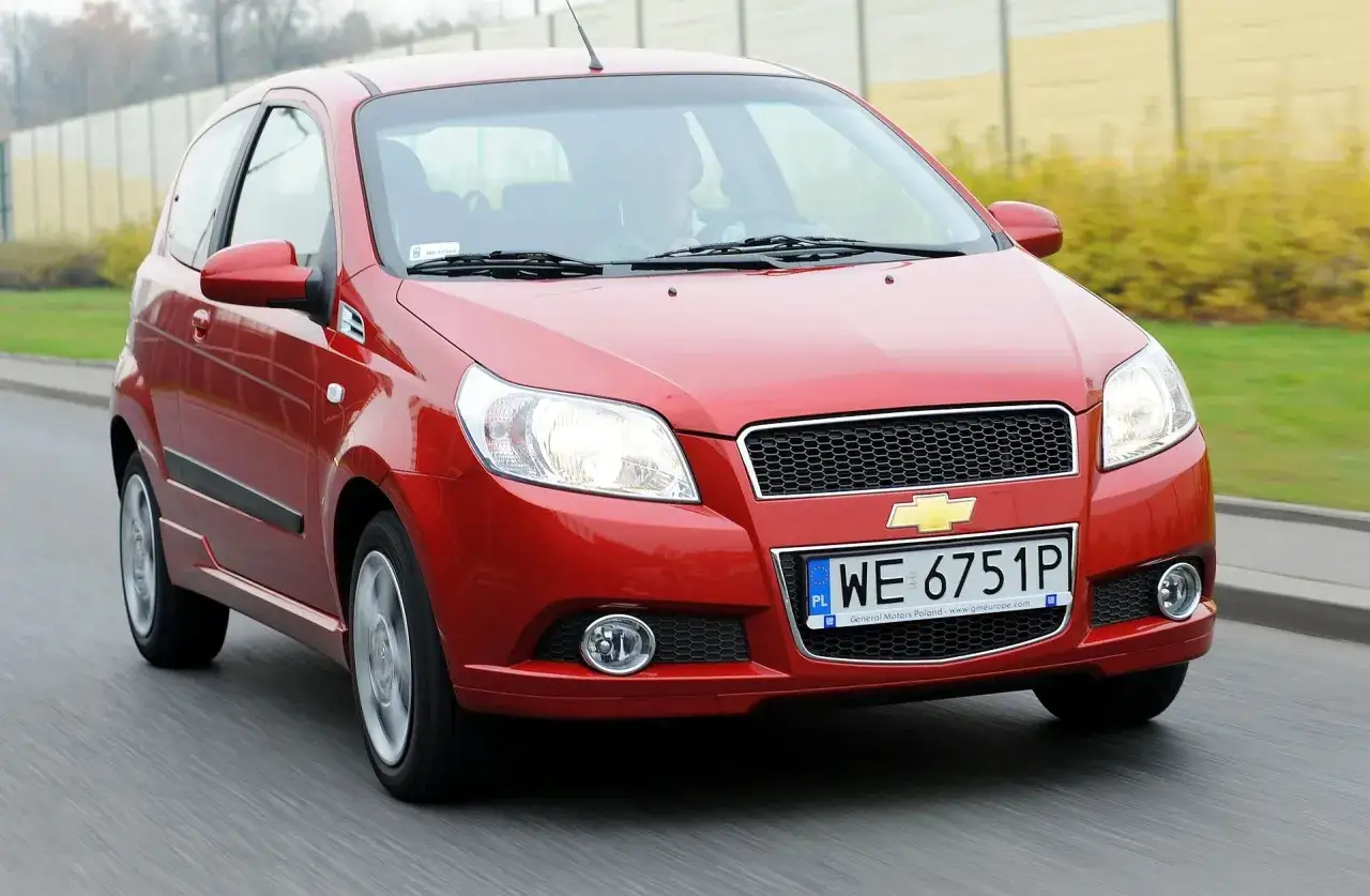 Czerwony Chevrolet Aveo z polskimi tablicami rejestracyjnymi WE 6751P jedzie po drodze.