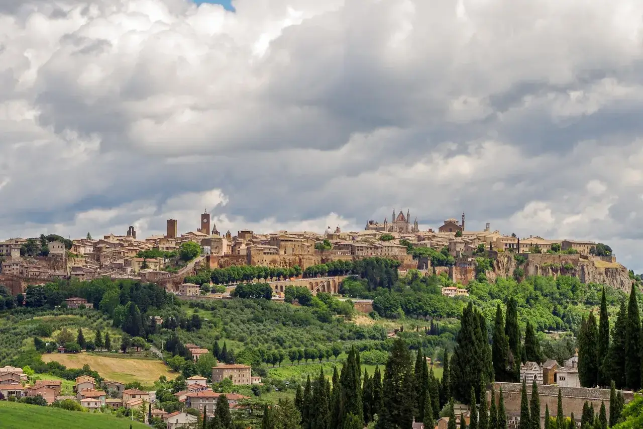 Panoramica di una citt&agrave; dell'Umbria arroccata su una collina, con edifici storici, un duomo imponente e vegetazione lussureggiante.