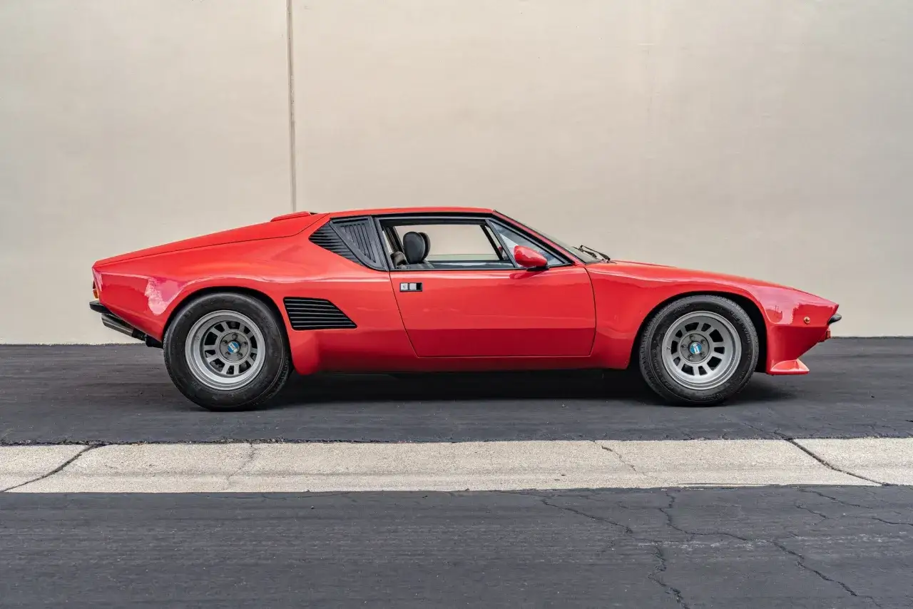 En röd De Tomaso Pantera bil parkerad framför en ljus vägg. Denna klassiska sportbil har en låg profil och aerodynamisk design.