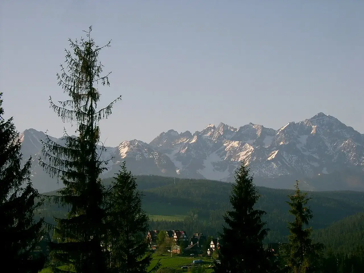Widok na Tatry z Bukowiny Tatrzańskiej, gdzie widać ośnieżone szczyty i lasy. W dole malownicze domy, idealne miejsce na narty.