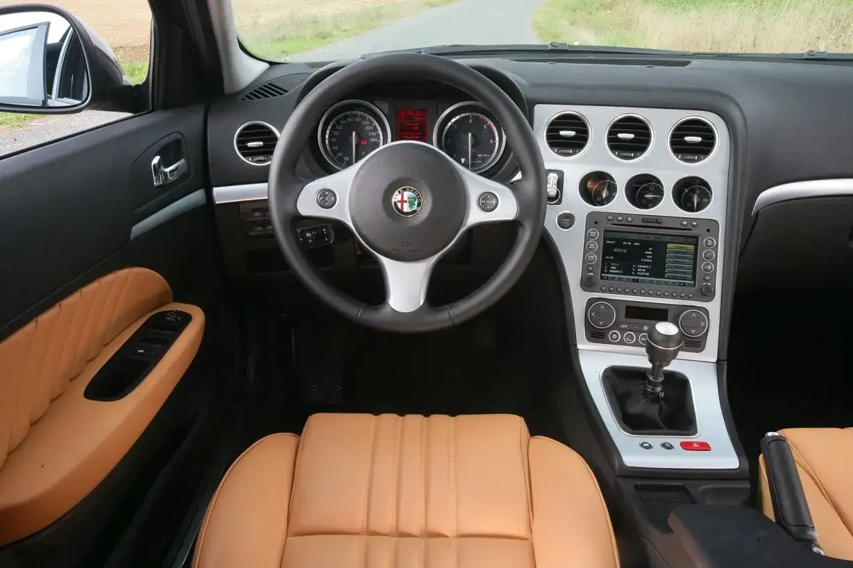 Wnętrze Alfa Romeo 159 1.9 JTD z beżową skórzaną tapicerką, kierownicą i panelem środkowym.