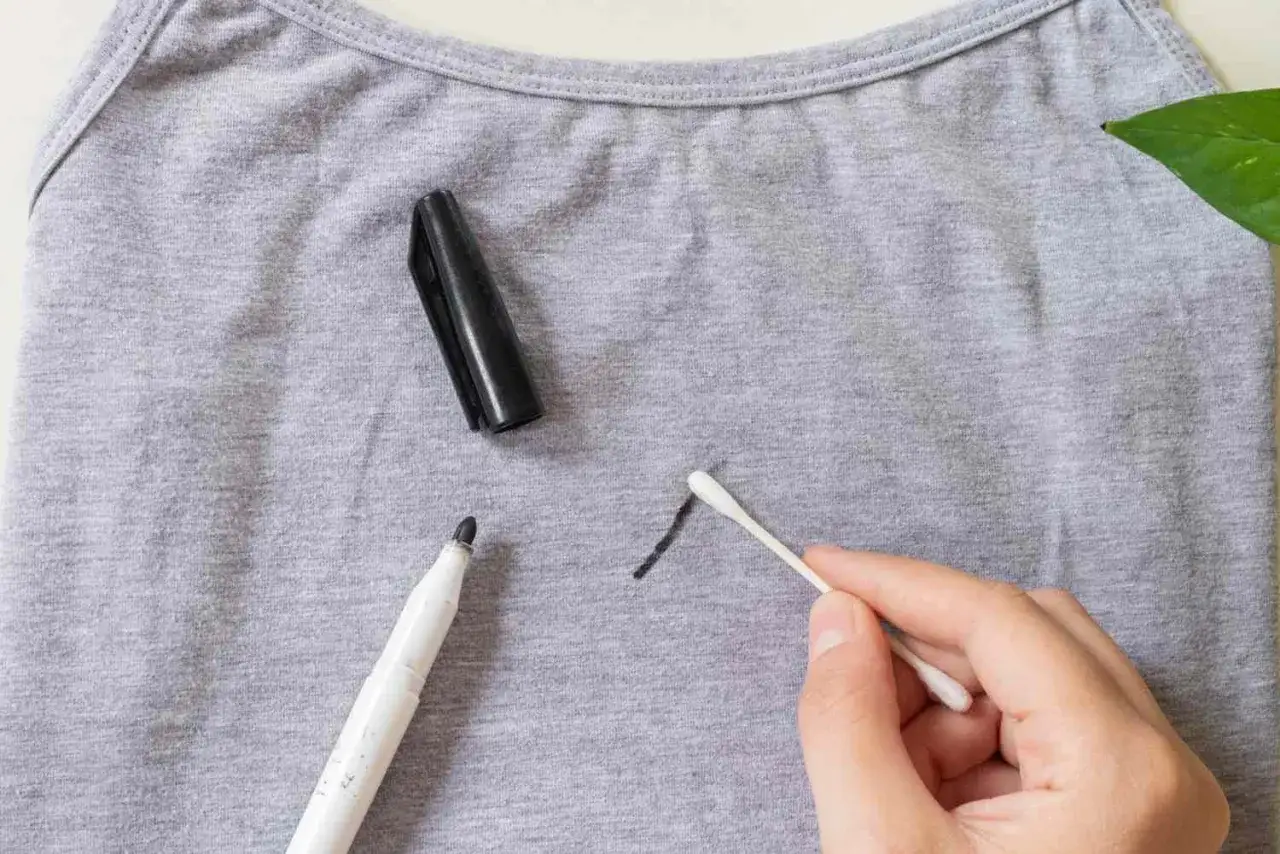 Un hisopo de algod&oacute;n limpia una mancha de rotulador seco en una camiseta gris.