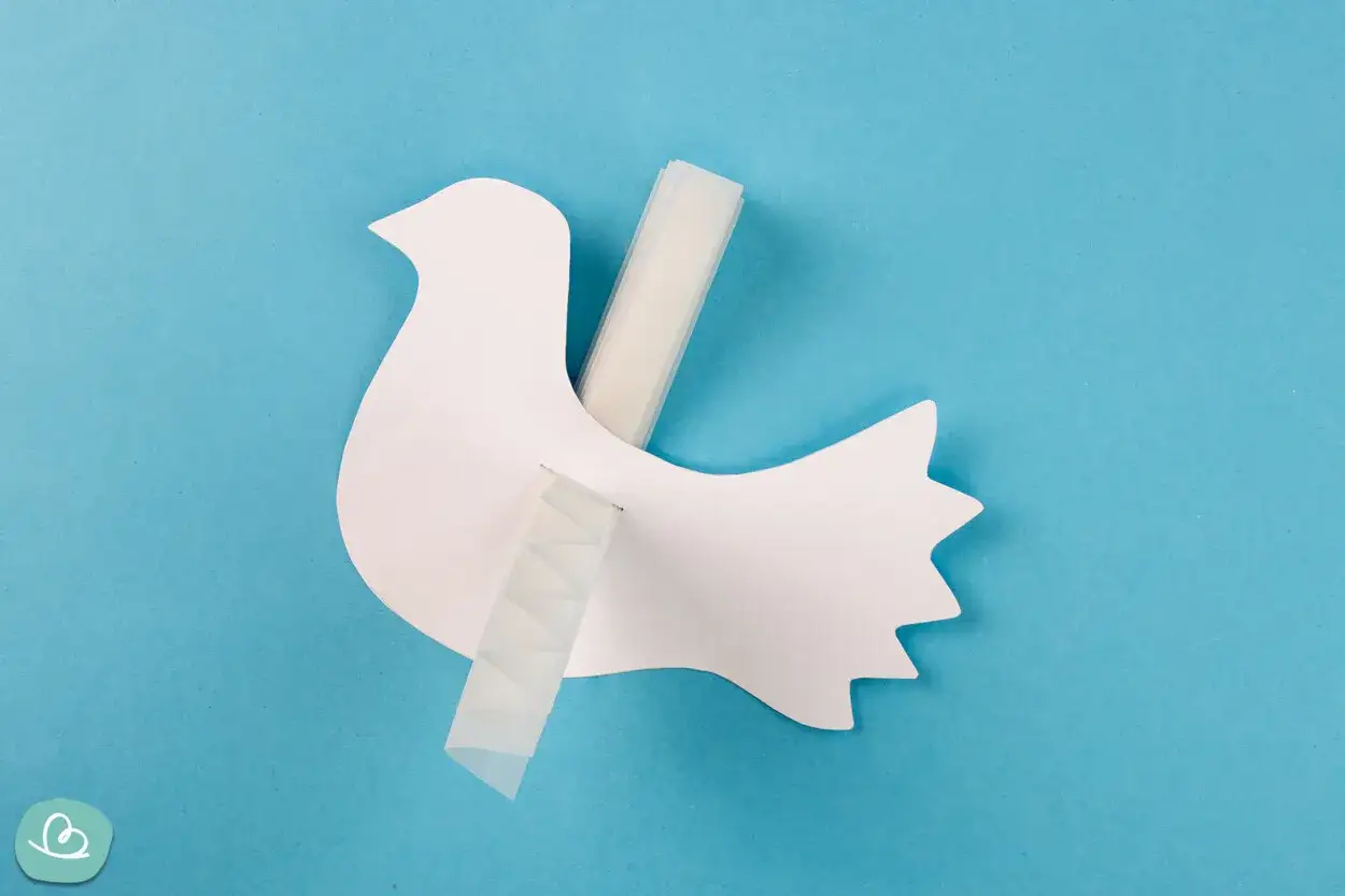 Eine weiße Papier-Friedenstaube wird mit Klebeband befestigt. Bastelanleitung für eine Friedenstaube.