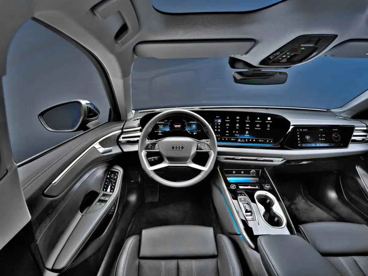Wnętrze Audi A6 2025: nowoczesny kokpit z dużymi ekranami, cyfrowym zegarem i sportową kierownicą.