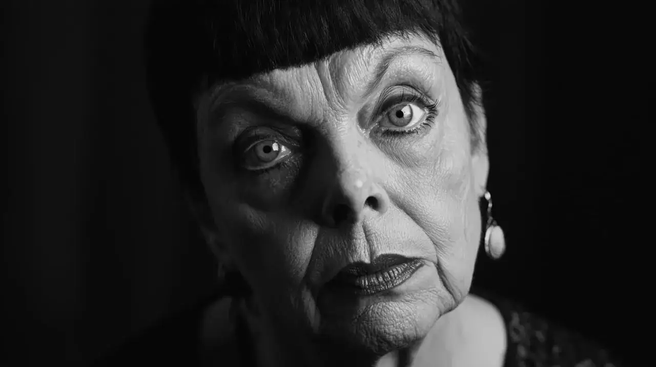 Intensywne spojrzenie kobiety na portrecie w stylu Diane Arbus. Jej zmarszczki i wyraziste oczy przyciągają uwagę.