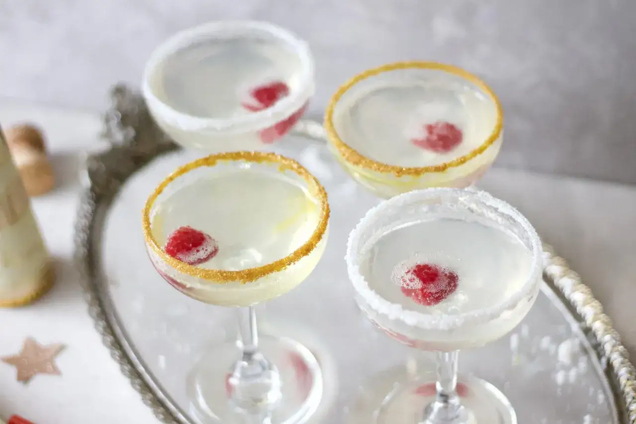 Cztery kieliszki z drinkami martini prosecco, ozdobione malinami i cukrem, gotowe na toast.
