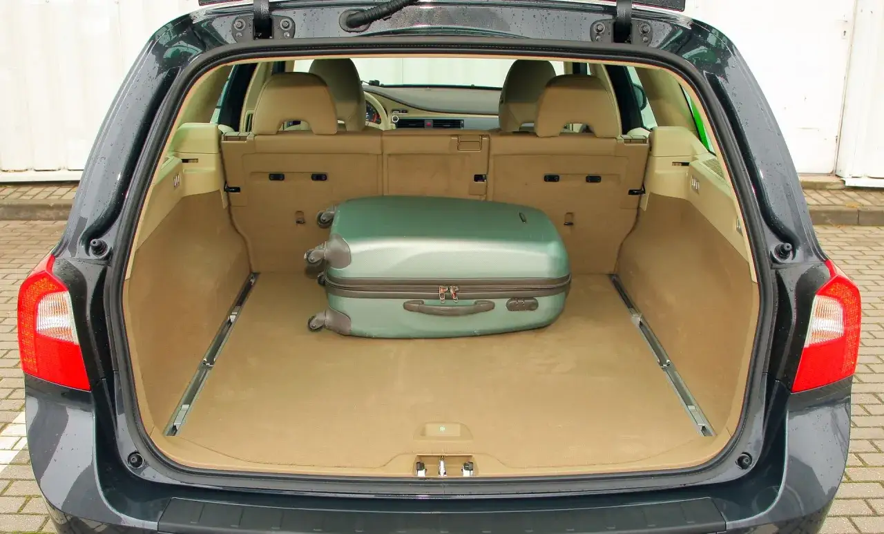 Bagażnik Volvo V70 II gotowy na podróż. Jedna zielona walizka czeka na załadunek.