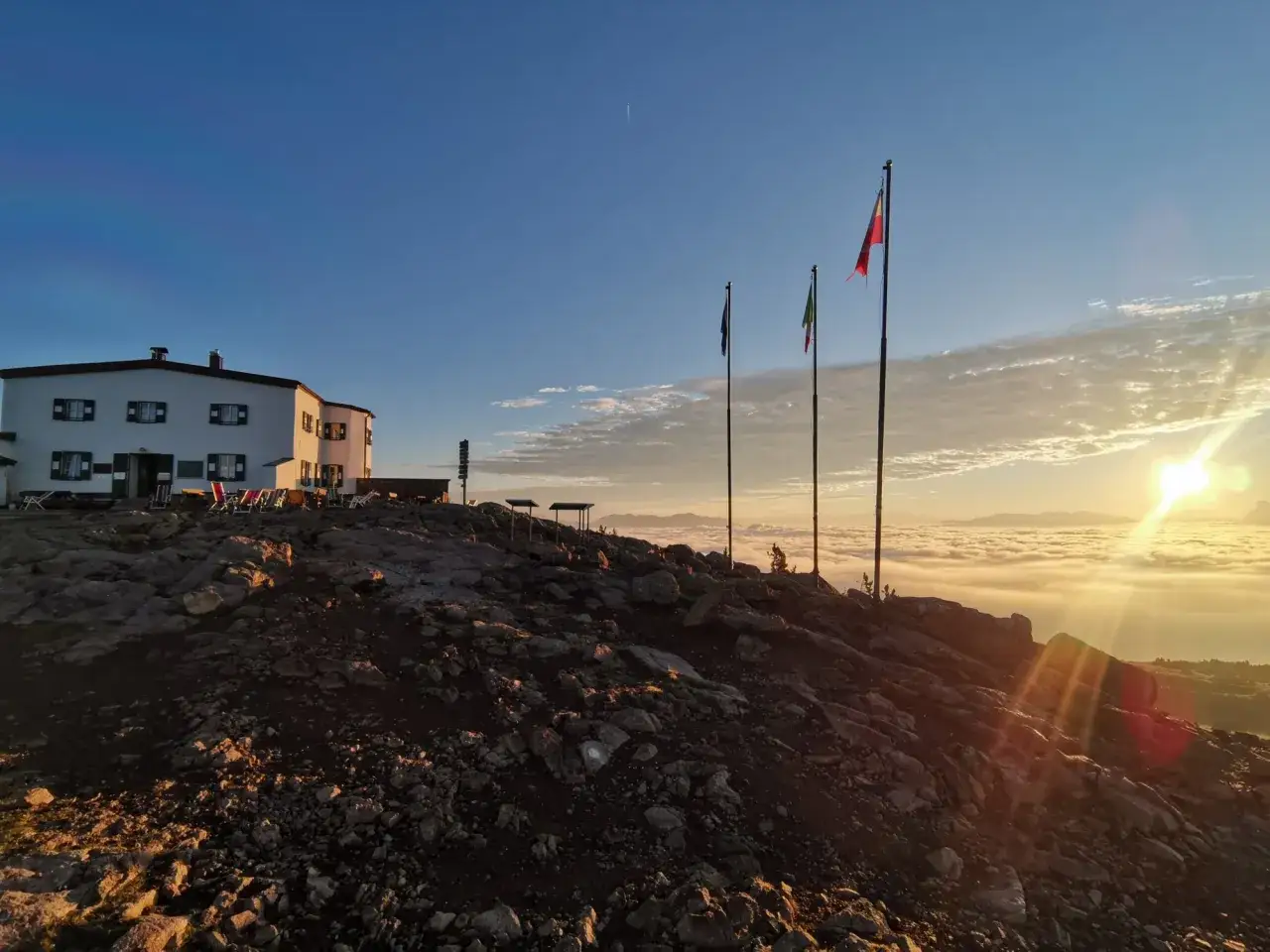 Sonnenaufgang über den Wolken auf der Sarntaler Hufeisentour. Berghütte mit Fahnen im goldenen Licht.