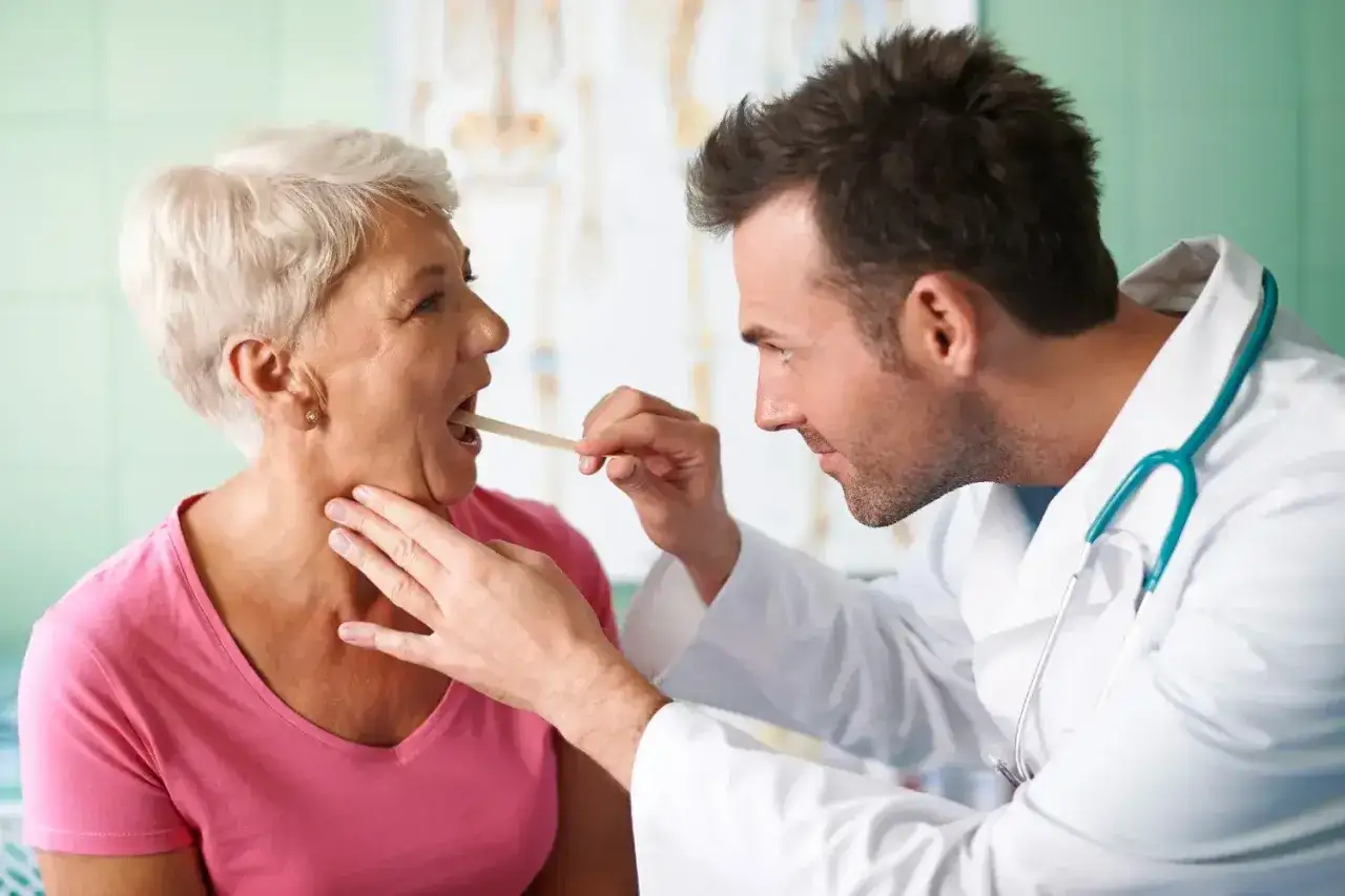 Lekarz bada gardło pacjentki drewnianym patyczkiem.