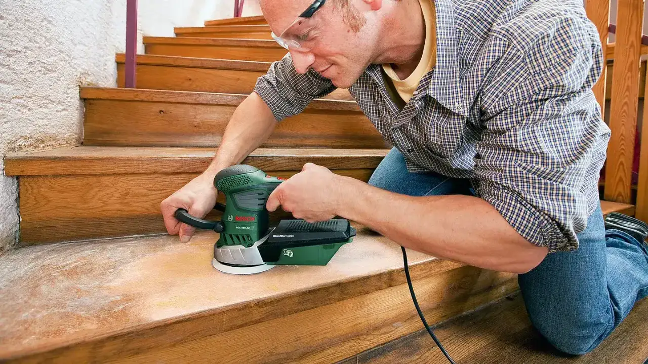 Un homme utilise une ponceuse escalier pour rénover des marches en bois.