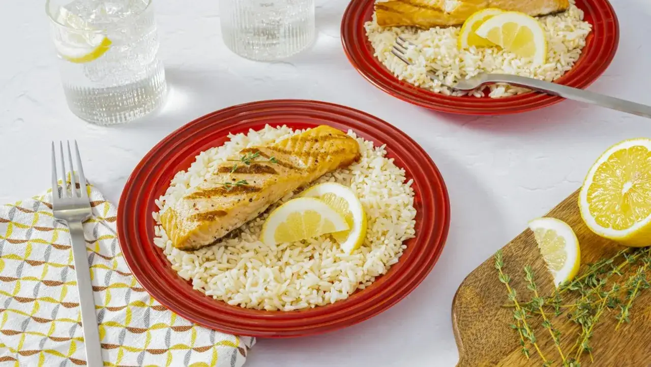 A perfectly grilled salmon shioyaki rests on a bed of fluffy rice, garnished with lemon slices and fresh thyme.
