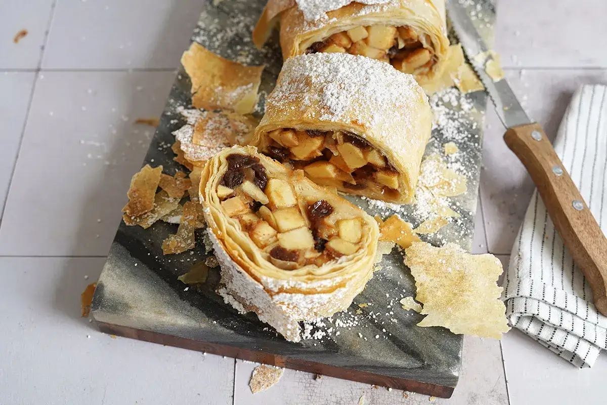 Ein k&ouml;stlicher Apfelstrudel mit Filoteig, best&auml;ubt mit Puderzucker, liegt auf einem Marmorbrett.