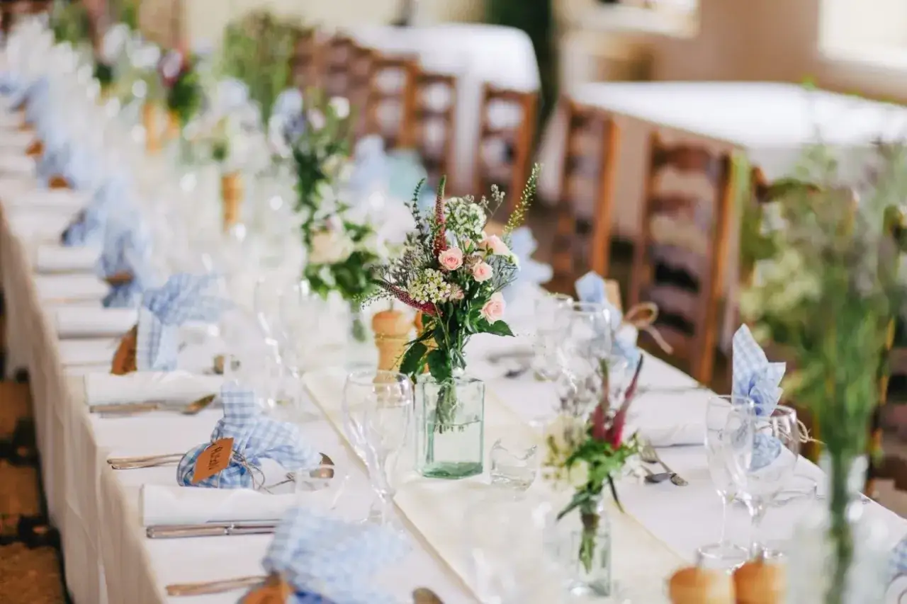 L'art de la table est célébré avec des bouquets champêtres, des serviettes à carreaux bleus et des verres à pied sur une longue table dressée pour une fête.