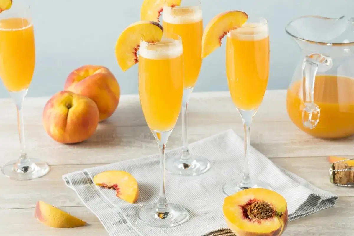 Letni poranek z brzoskwiniowym nektarem i prosecco. Czy to Mimosa czy Bellini? Kilka kieliszków z pianką, świeże brzoskwinie i dzbanek napoju.