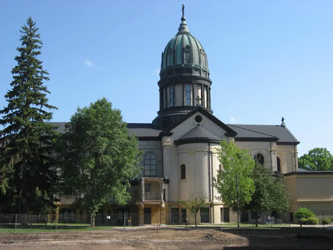 The grand dome of Saint Benedict's Monastery stands tall against a clear blue sky, surrounded by lush green trees.