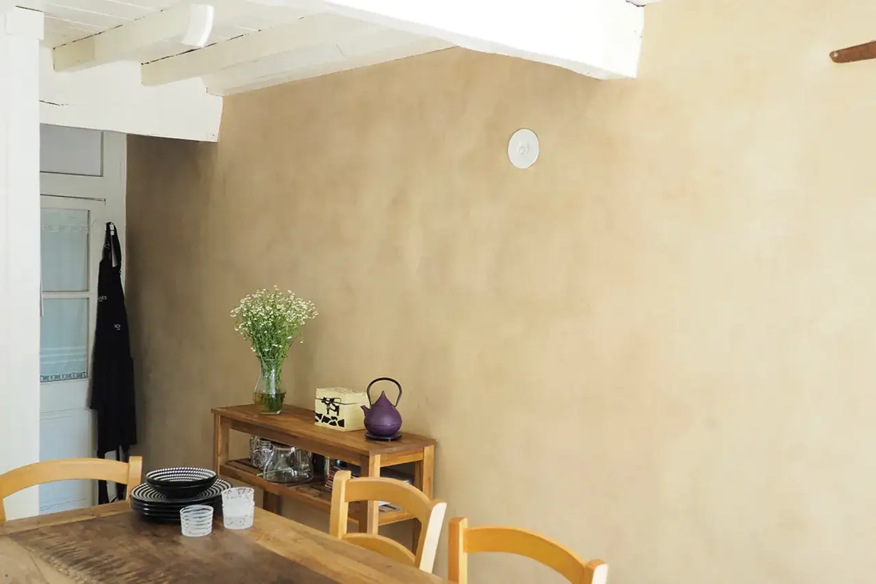 Un mur &agrave; la texture douce, comme une peinture sur argile, habille cette salle &agrave; manger. Des fleurs et des objets d&eacute;coratifs sur une &eacute;tag&egrave;re en bois.