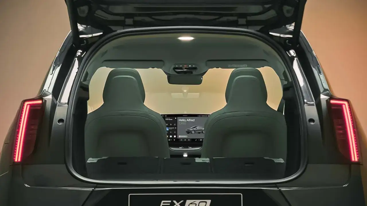 Interno del bagagliaio aperto di una Volvo EX60, con sedili posteriori in pelle verde e un grande schermo centrale che mostra 