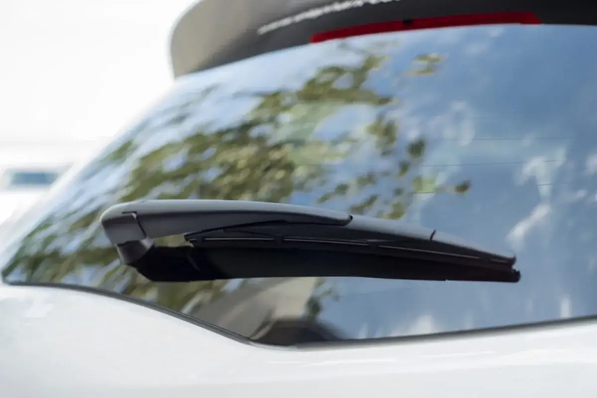 Nahaufnahme eines Heckscheibenwischers, bereit zum Wechseln. Der Wischerarm ist schwarz und liegt auf der Heckscheibe eines weißen Autos.