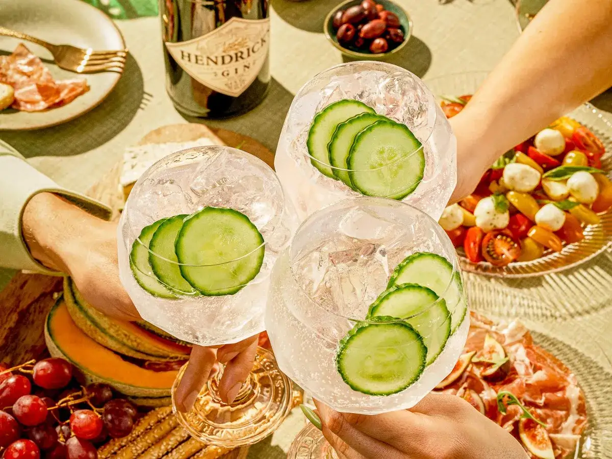 Drei Gläser Gin Tonic mit Gurkenscheiben stoßen an. Eine Flasche Hendricks Gin steht bereit.