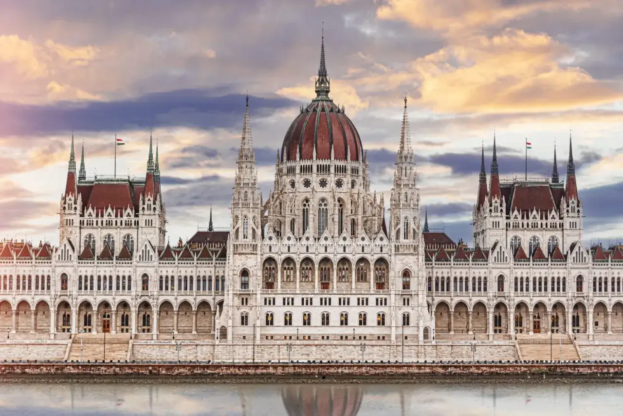 Majestatyczny Parlament w Budapeszcie, jeden z głównych punktów, co zobaczyć w Budapeszcie, odbija się w spokojnej wodzie Dunaju.
