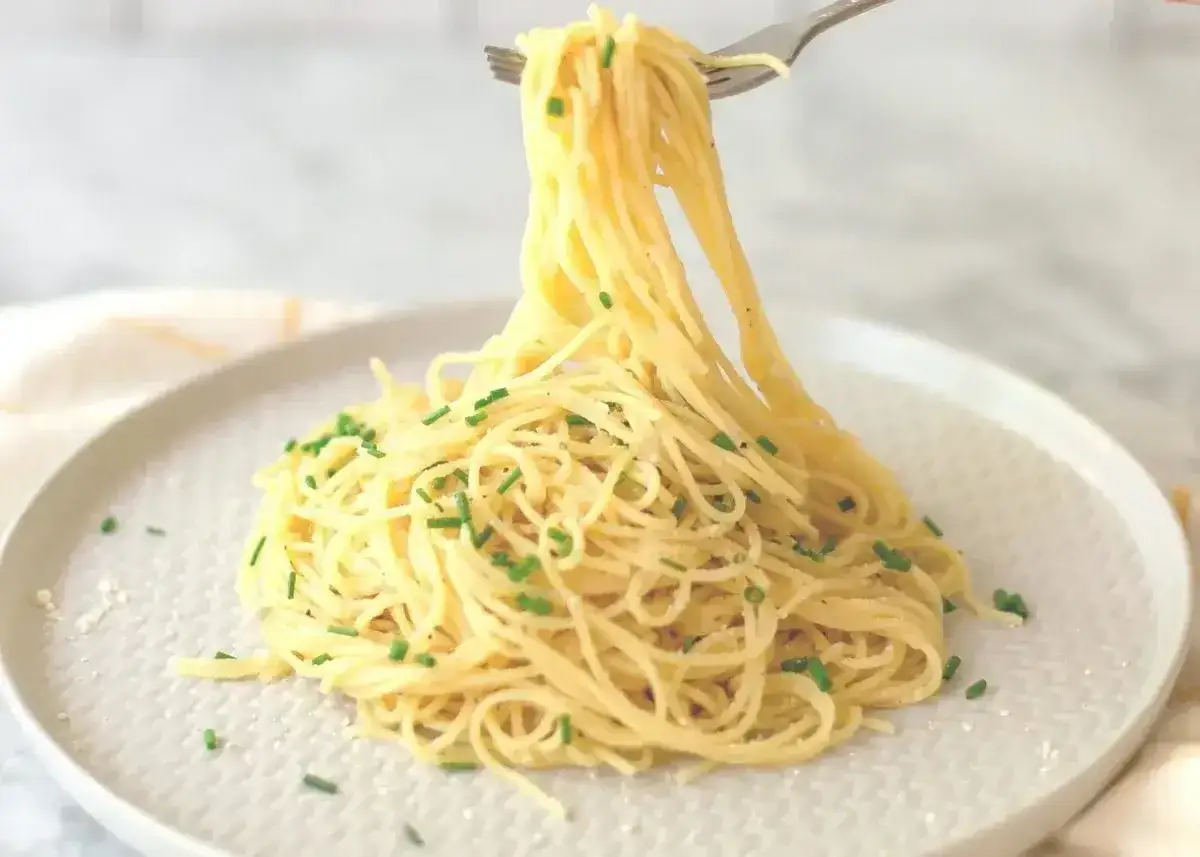 Pyszne dania z parmezanem: widelcem nabierane spaghetti z posiekanym szczypiorkiem, posypane parmezanem.