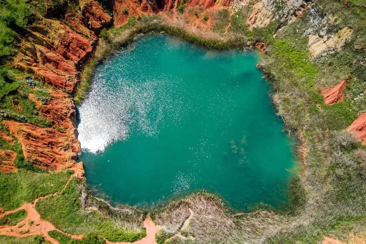 Lago turchese circondato da rocce rosse e vegetazione rigogliosa, un paesaggio suggestivo che ricorda le cave di bauxite.