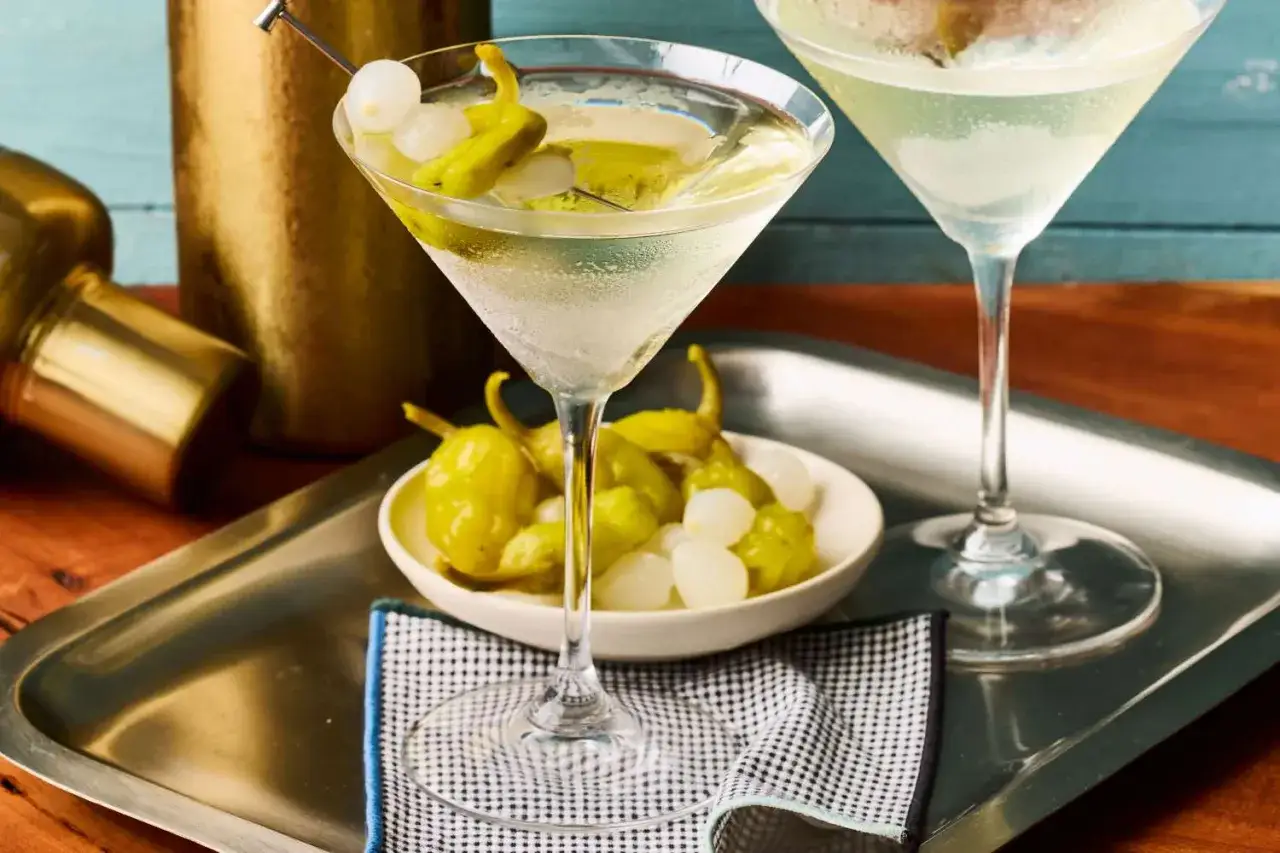 Dwa kieliszki martini z oliwkami i papryczkami, obok miseczka z dodatkami. Idealne, by poczuć, jak smakuje martini.