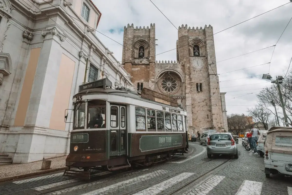 Lizbona grudzień, pogoda pochmurna. Zabytkowy tramwaj jedzie ulicą obok katedry.