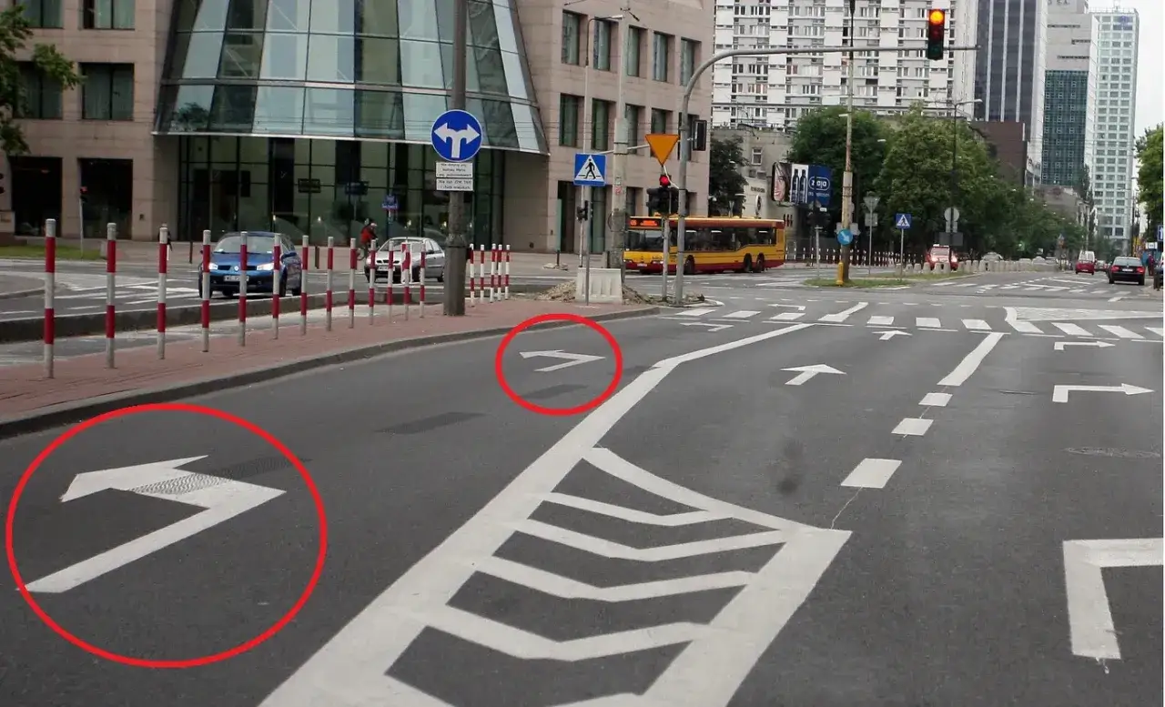 Strzałki na jezdni wskazują dozwolone kierunki jazdy, w tym możliwość **zawracania**. Widać też autobus i samochody.