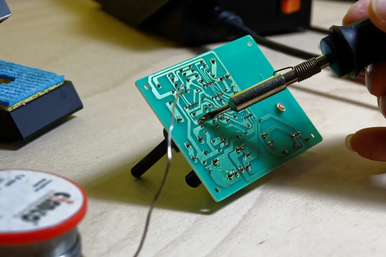 Mano che salda una scheda elettronica con stagno. Si possono saldare componenti su circuiti stampati, fili e connettori.