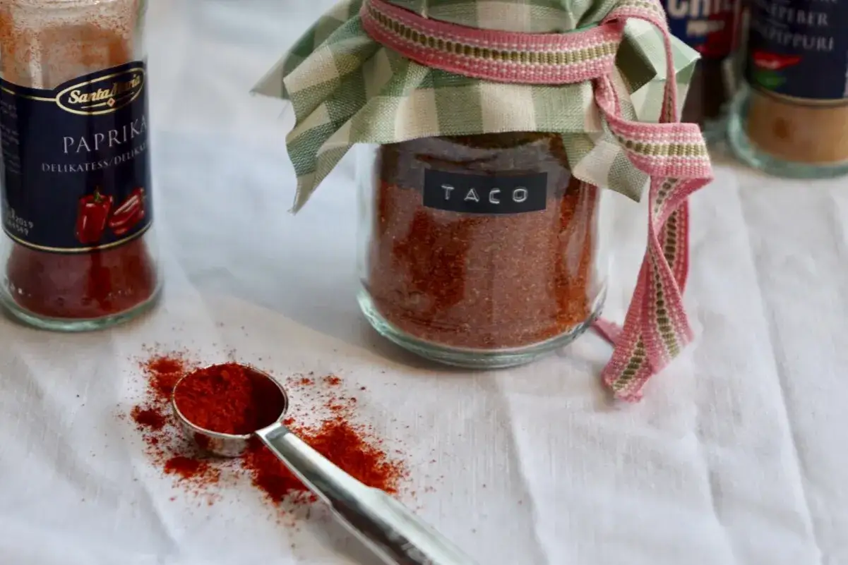 En burk med hemmagjord tacokrydda, perfekt för att göra ditt eget tacokrydda recept. En skopa med kryddblandning ligger bredvid.