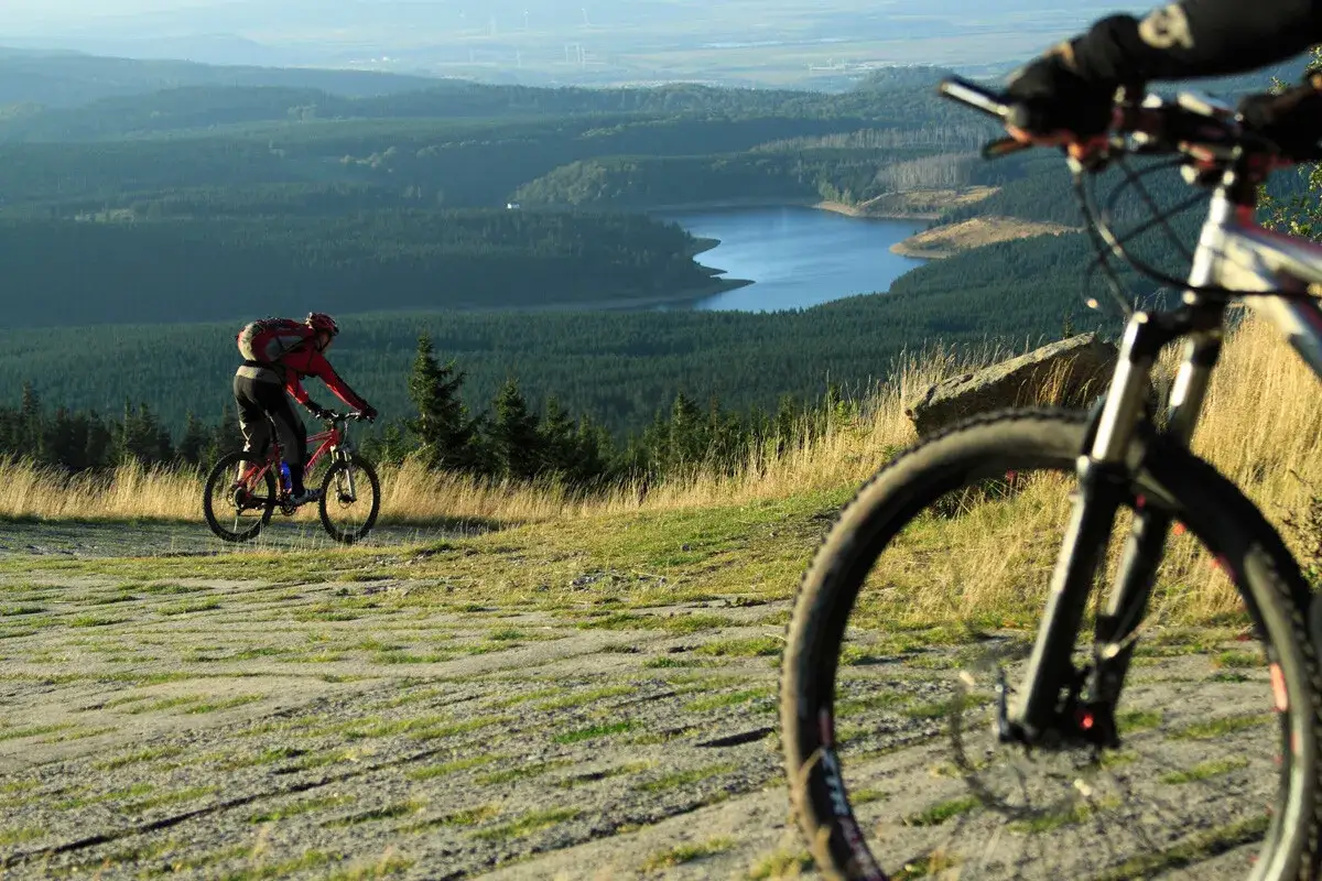 Zwei Radfahrer genießen eine atemberaubende Aussicht bei ihren MTB Touren. Ein See und Wälder erstrecken sich in der Ferne.