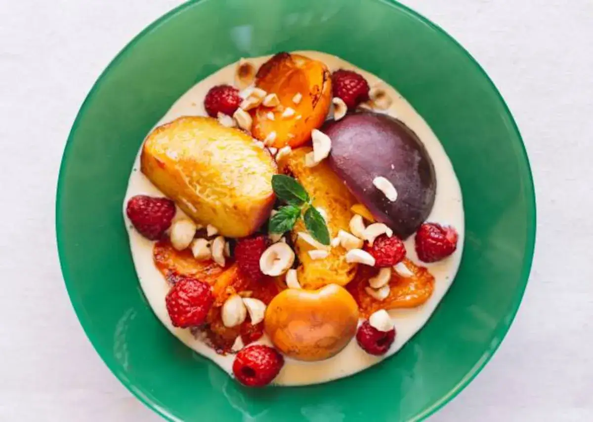 Frutas asadas con frambuesas, nueces y una generosa porci&oacute;n de crema inglesa en un plato verde.