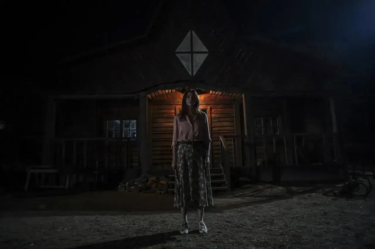 Una donna in piedi davanti a una casa isolata di notte. L'atmosfera evoca una classica storia horror, con un'inquietante spiegazione in agguato.