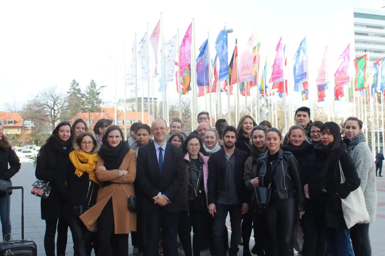 Groupe d'étudiants souriants devant des drapeaux, prêts pour leur future carrière dans une école de tourisme gratuite.