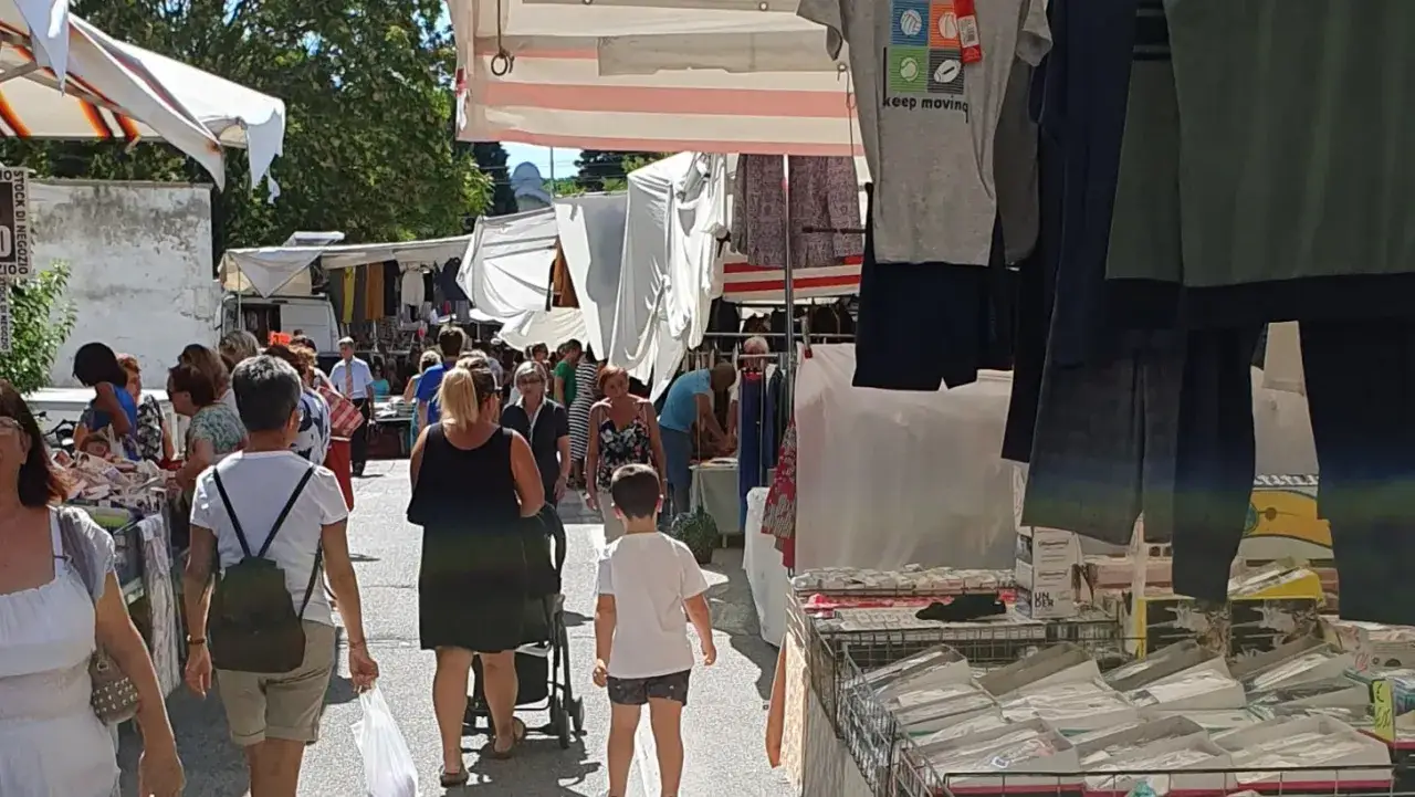Gente passeggia tra le bancarelle del mercato di Porto San Giorgio, tra abiti e mercanzie esposte sotto i tendoni.