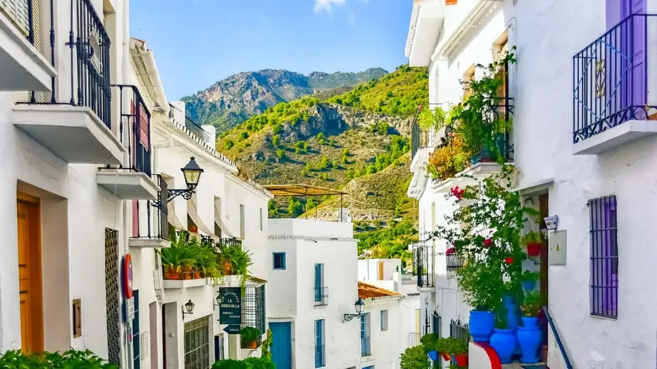 Calle empedrada en un pintoresco pueblo blanco andaluz, uno de los pueblos cerca de Málaga, con montañas verdes al fondo.