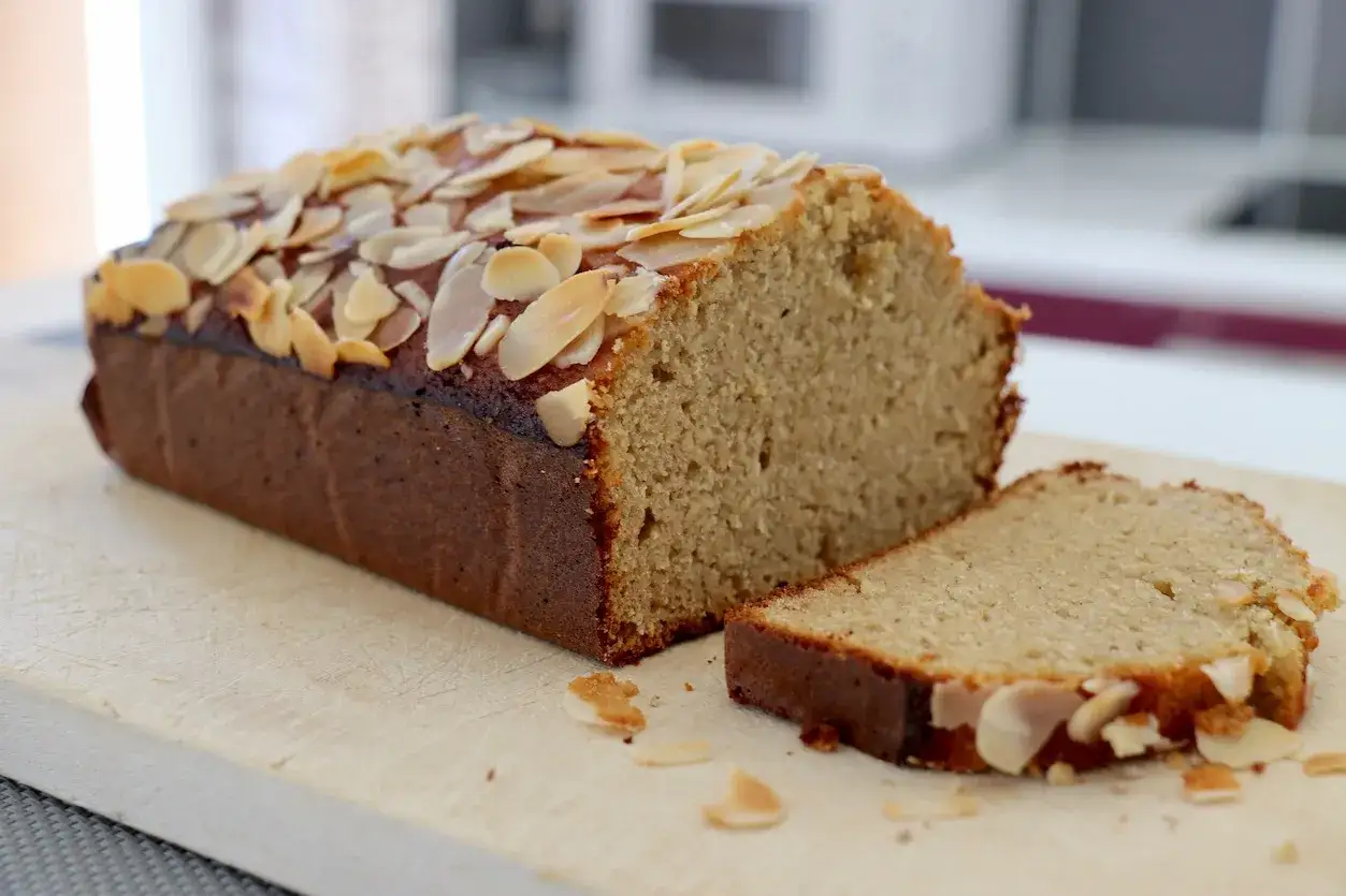 Un d&eacute;licieux g&acirc;teau sans gluten, garni d'amandes effil&eacute;es, est coup&eacute; en tranches sur une planche en bois.