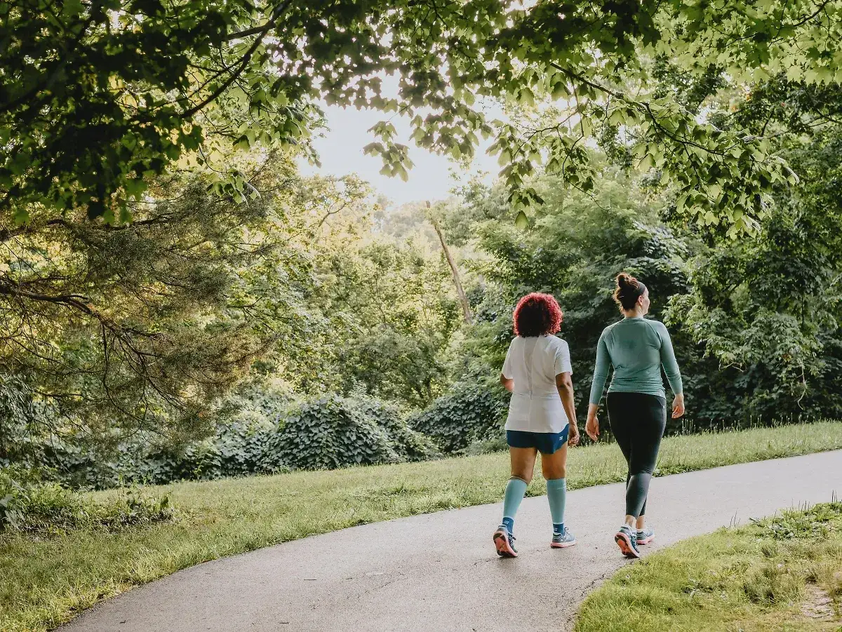 Zwei Frauen joggen auf einem Weg im Grünen. Sie genießen die frische Luft und die Natur. Was bringt joggen? Gesundheit und Wohlbefinden!