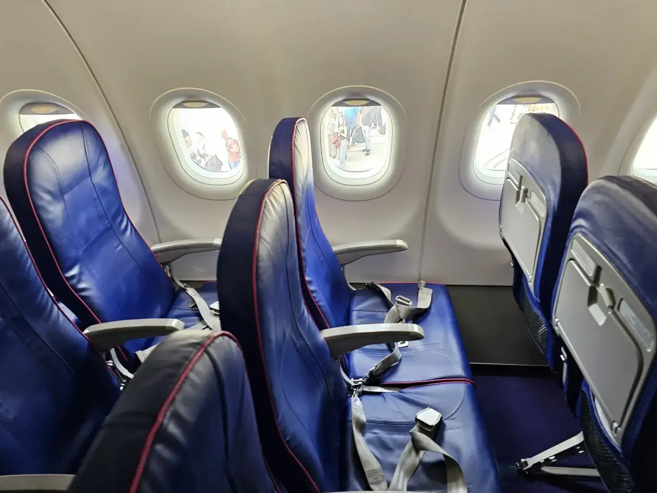 Puste siedzenia w samolocie Wizzair, przez okna widać ludzi czekających na odprawę.