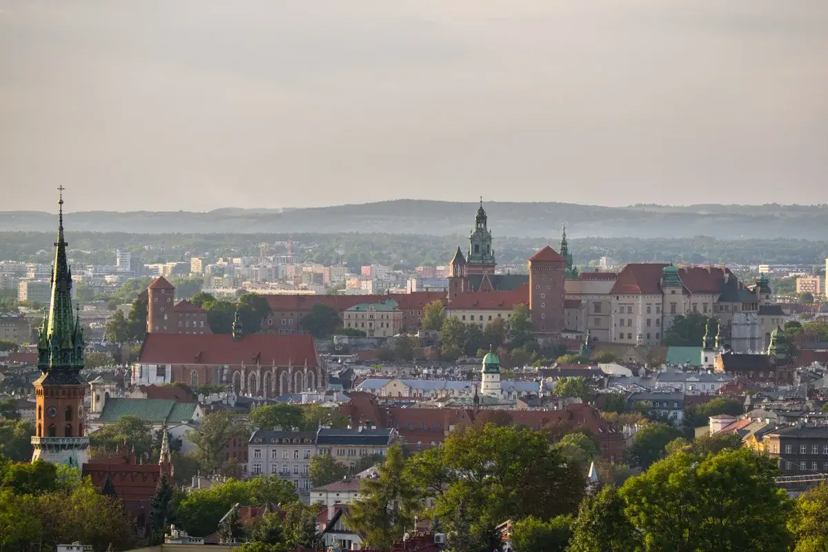 Widok na Wawel i inne zabytkowe kopce w Krakowie, z zielonymi wieżami i ceglanymi murami, w otoczeniu miejskiej panoramy.