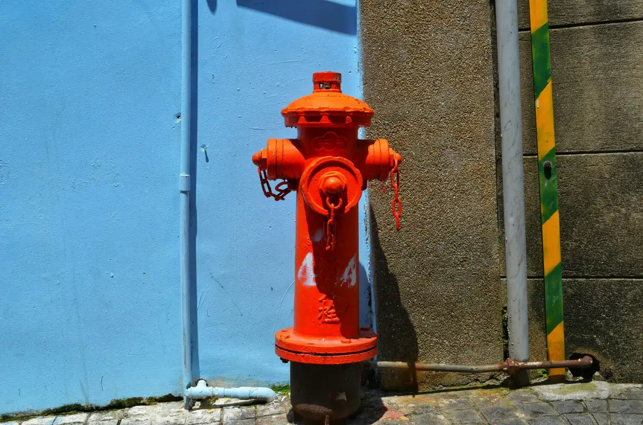 Ein roter Hydrant, der erklärt, was ein Hydrant ist, steht vor einer blauen Wand.